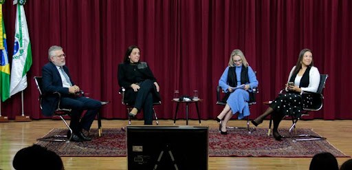 Fotografia de um grupo de pessoas posando para foto no palco de um auditório. Um homem e uma mul...