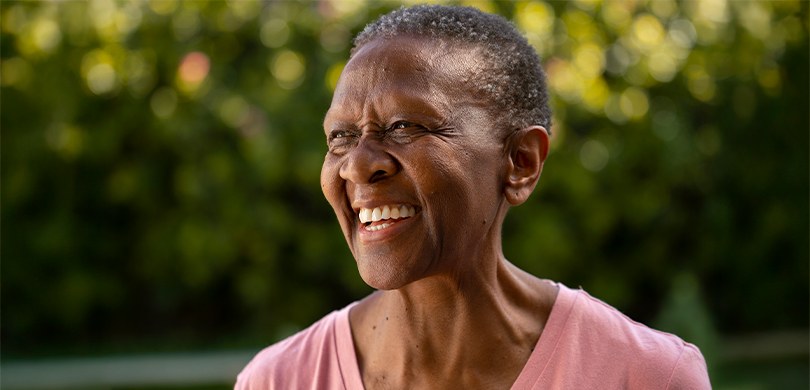 Fotografia em que se observa, em primeiro plano e em meio-perfil, uma mulher idosa de pele retin...