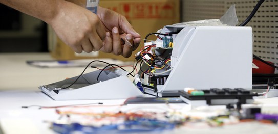 Participantes do TPS ajudam a promover inovações importantes no sistema eletrônico de votação Foto de uma urna sendo montada por dentro por duas mãos