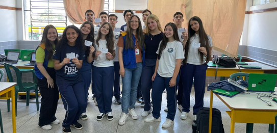 Fotografia de uma mulher em pé palestrando para jovens uniformizados em uma sala de aula com par...