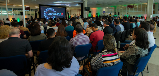 A Diretora-Geral Solange Maria Vieira fala para a plateia segurando um microfone. Atrás dela, um...