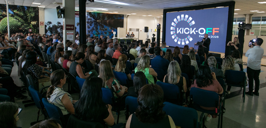 A Diretora-Geral Solange Maria Vieira fala para a plateia segurando um microfone. Atrás dela, um...