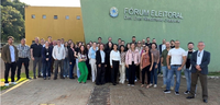 Fotografia de diversas pessoas, entre homens e mulheres, posando sorrindo em frente ao Fórum Ele...