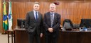 Fotografia de dois homens trajando ternos escuros em frente à mesa da sala de sessões do TRE-PR....