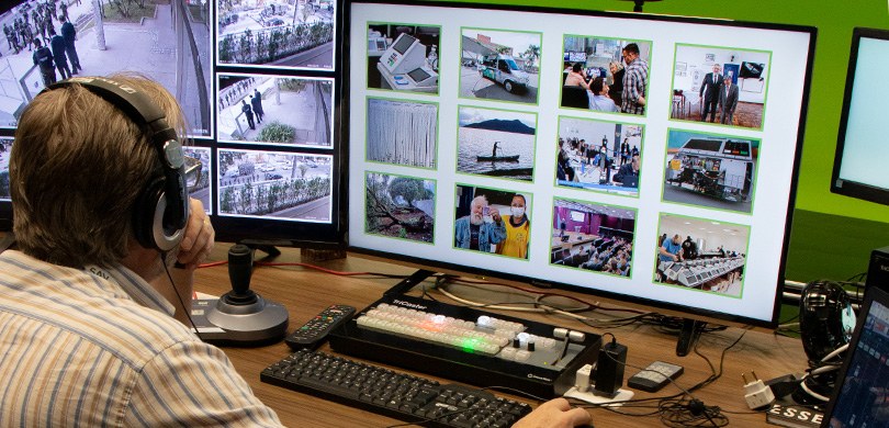 Fotografia de um homem de costas, olhando para dois monitores com imagens relacionadas à eleição...