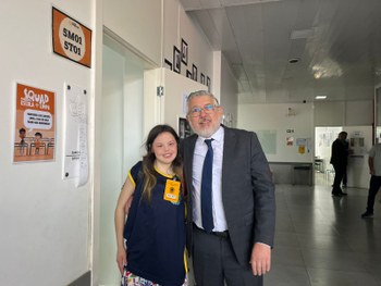 Fotografia de um homem de terno e gravata parado ao lado de uma cabina de votação em uma sala de...