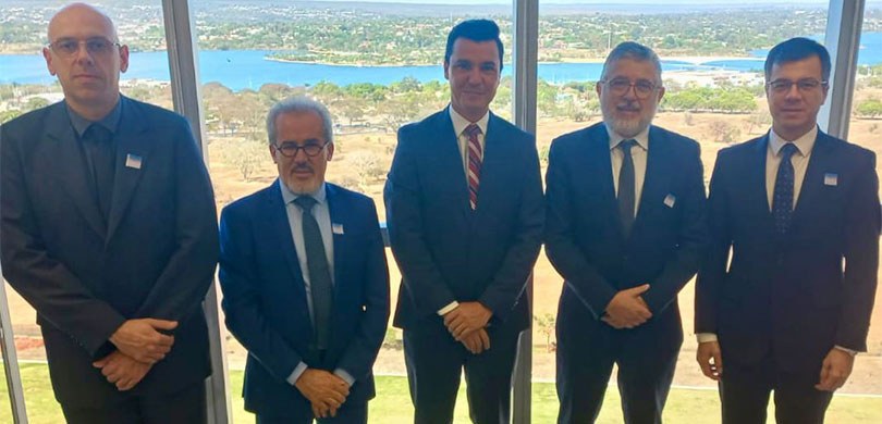 Fotografia de cinco homens de terno e gravata. Eles estão em pé, lado a lado, em frente a uma ja...