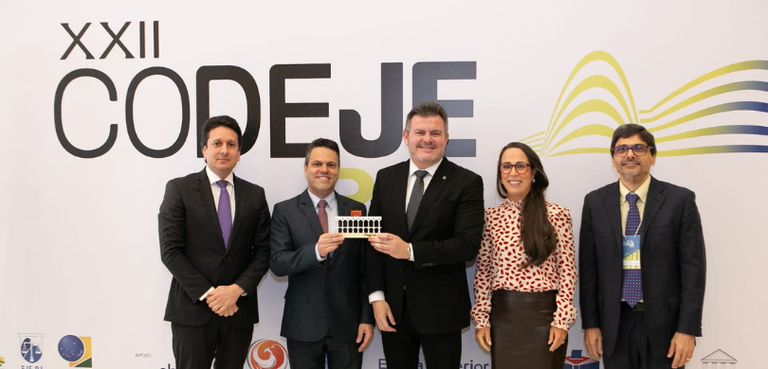 Presidente do TRE-PR e diretor-executivo da EJE-PR recebem homenagem no XXII Codeje 4 Fotografia de quatro homens de terno e uma mulher, com camisa estampada e saia de couro marrom, ...