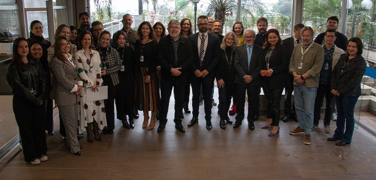 Presidente do TRE-PR empossa novos assessores 2 Fotografia de um grupo de diversas pessoas posando sorrindo. Ao fundo, diversas árvores e plantas.