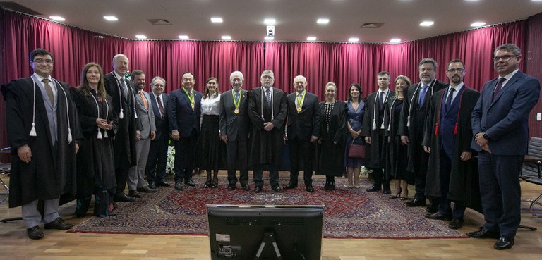 Fotografia de 17 pessoas, entre homens e mulheres, posando sorrindo em um palco de auditório. To...