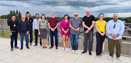 Grupo de 11  pessoas posando para foto, sendo três mulheres e oito homens. Ao fundo, é possível ...