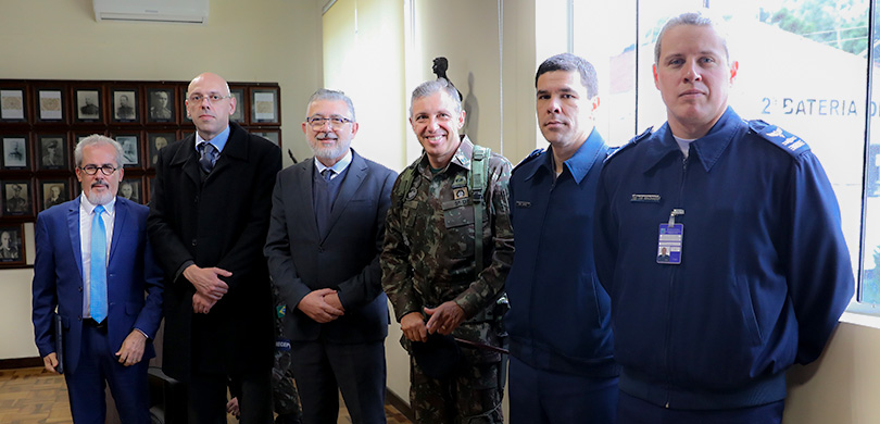 Fotografia de seis homens em pé, três usam terno, um está vestindo farda e outros dois com unifo...