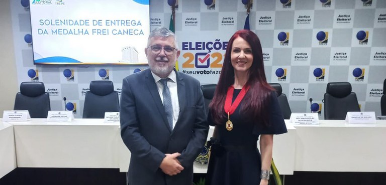 Fotografia de um homem de terno e de uma mulher ruiva e com vestido preto posando sorrindo para ...