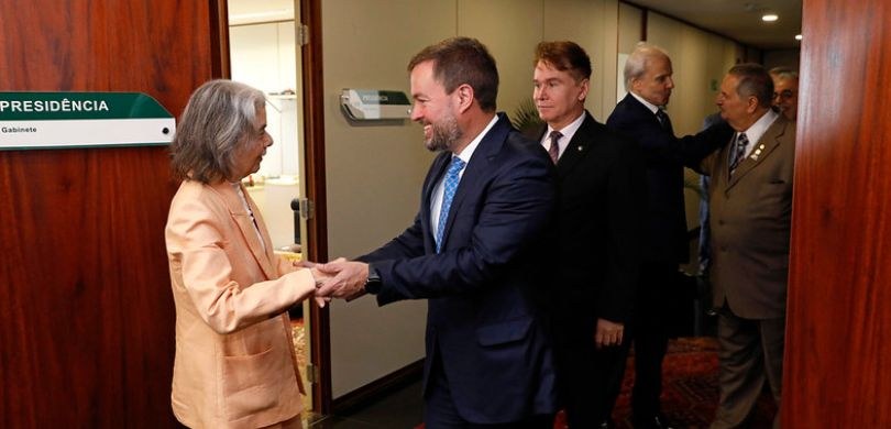 Fotografia que retrata um encontro entre diversas pessoas em um ambiente interno de um prédio in...