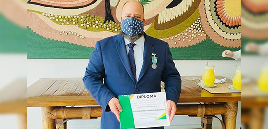 Foto do coordenador de Segurança do TRE-PR, Flávio Marçal, com a medalha e o diploma recebidos n...
