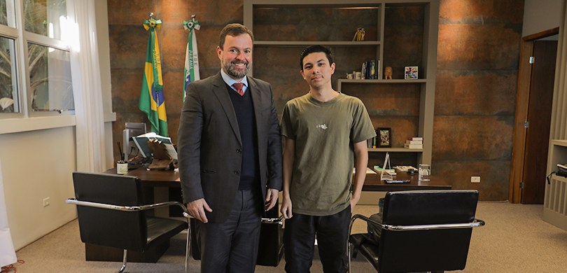 Fotografia em que se observam dois homens em pé, posando lado a lado para a foto no interior de ...
