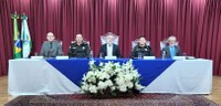 Fotografia da mesa de autoridades do evento, no palco do auditório do TRE-PR. Cinco homens apare...