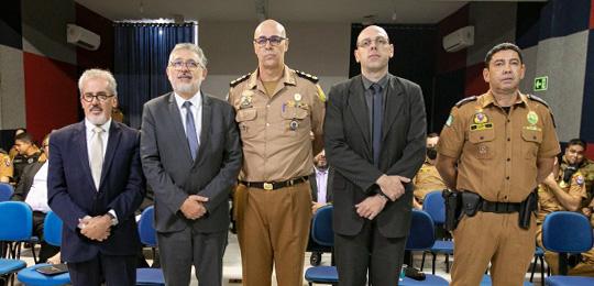 Foptografia de cinco homens posando para foto. Três deles usam terno e os outros dois estão fard...