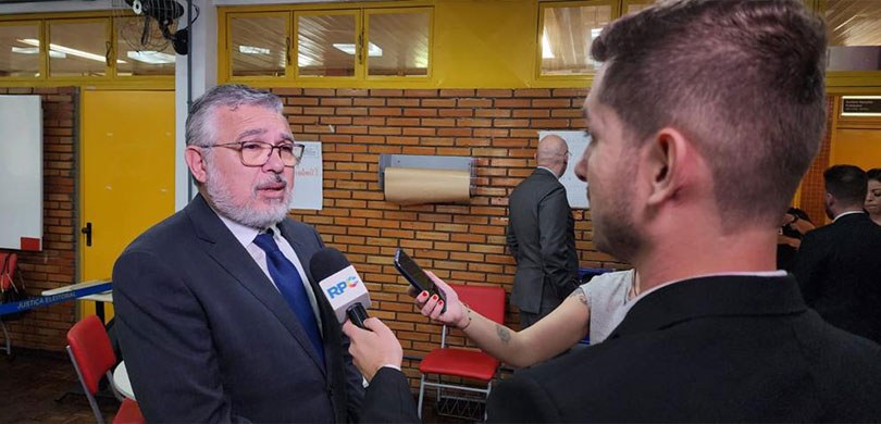Fotografia de um homem de terno e gravata concedendo entrevista para jornalistas.