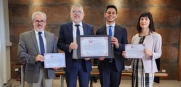 Fotografia de quatro pessoas, uma mulher e três homens, posando sorrindo para foto. Os dois home...