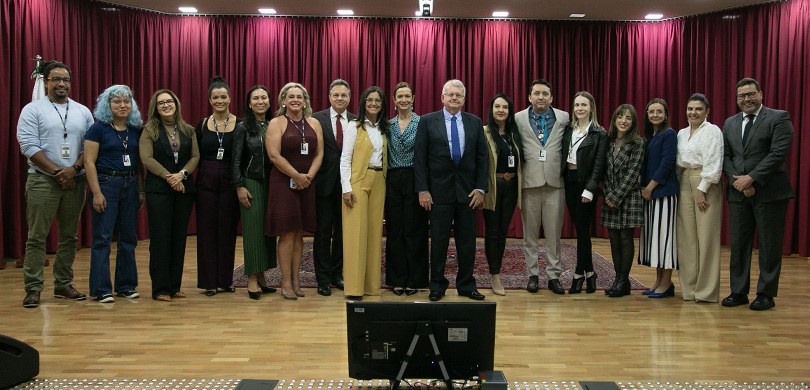 Fotografia de diversas pessoas, entre homens e mulheres, posando sorrindo em um palco de auditór...
