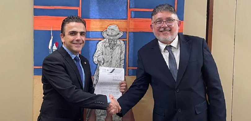 Fotografia de dois homens de terno se cumprimentando enquanto sorriem para a câmera. Um deles se...