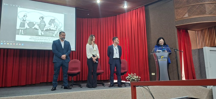 Fotografia em que se observam quatro pessoas num palco de um auditório. Da esquerda para a direi...