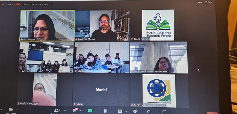 Foto de uma tela, em que se vêem servidores do TRE-PR, alunos em escolas e o palestrante em uma ...