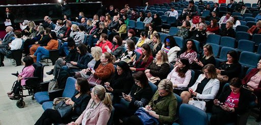 Fotografia de um grupo de pessoas posando para foto no palco de um auditório. Um homem e uma mul...