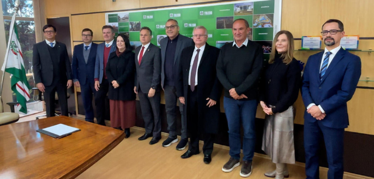 Fotografia de duas mulheres, que usam roupas formais, e oito homens de terno posando sorrindo em...