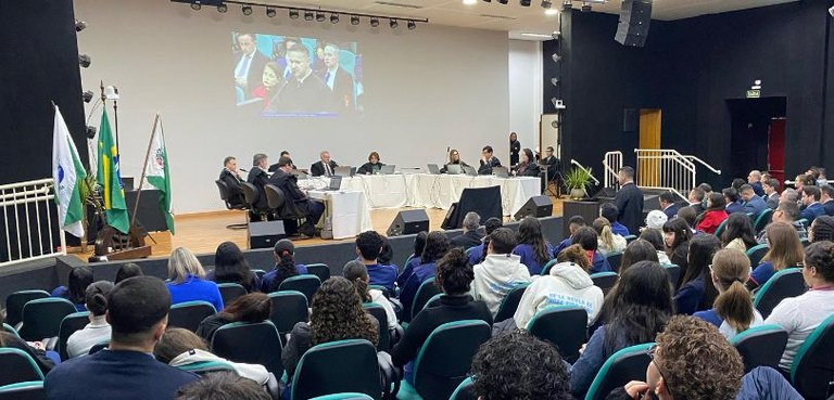 Fotografia da Corte do TRE-PR sentada em cadeiras pretas, de frente para uma mesa, sobre a qual ...