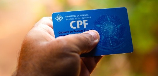 Fotografia de uma mão masculina segurando um documento de CPF