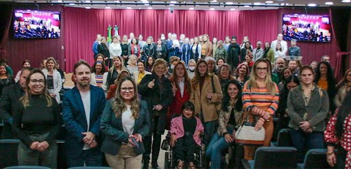 Fotografia de um grupo de pessoas posando para foto no palco de um auditório. Um homem e uma mul...
