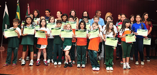 Crianças uniformizadas segurando um diploma nas mãos cada uma