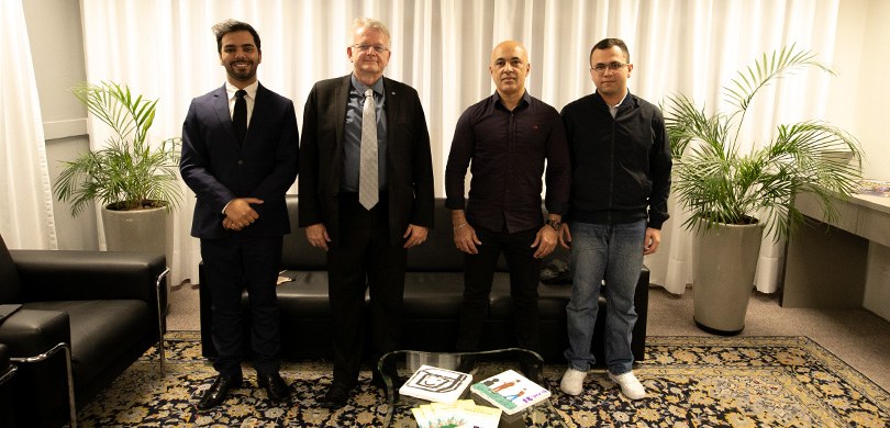 Representantes da organização Transparência Eleitoral Brasil visitam o TRE-PR Em uma sala com paredes e cortinas brancas, quatro homens posam para a foto. Eles estão em cima ...