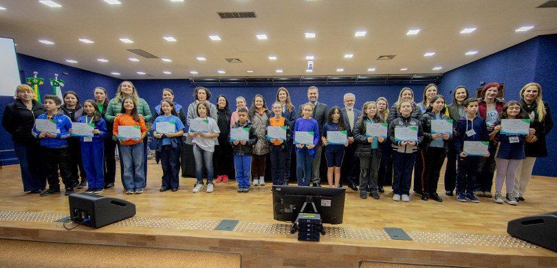 Fotografia em ambiente interno que retrata um grupo composto por crianças e adultos posando alin...