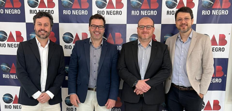 Representantes do TRE-PR participam do evento “Justiça, Democracia e Eleições”, em Rio Negro (PR) Fotografia de quatro homens posando em frente a um banner da OAB - Subseção de Rio Negro, nas co...