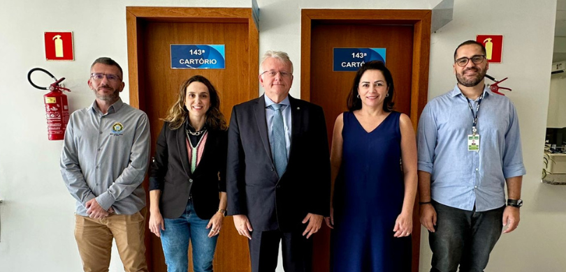 Fotografia de três homens e duas mulheres posando sorrindo. Eles vestem roupas formais nas cores...