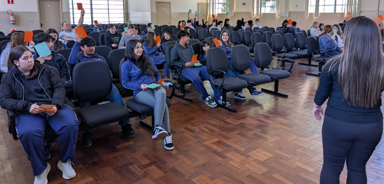 Fotografia de uma mulher em pé palestrando para jovens uniformizados em uma sala de aula com par...