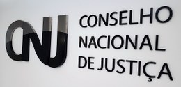 Fotografia de uma parede branca, escrito em preto: CNJ - Conselho Nacional de Justiça.