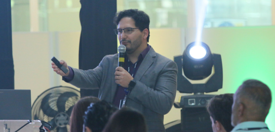 Fotografia de nove pessoas, entre homens e mulheres, posando sorrindo em frente a um edifício co...