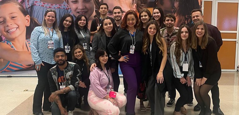 Fotografia de um grupo de 17 pessoas, entre homens e mulheres, posando sorrindo, alinhadas em tr...