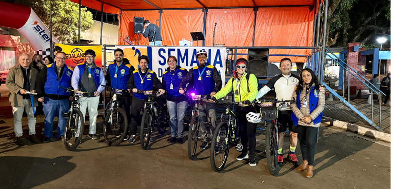 Fotografia, tirada à noite, de diversas pessoas, entre homens e mulheres, posando sorrindo com a...
