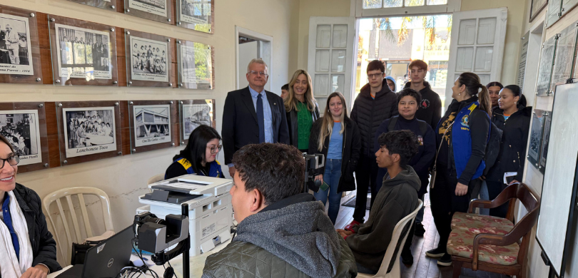 Fotografia de diversas pessoas, entre homens e mulheres, em uma sala com paredes na cor creme. E...