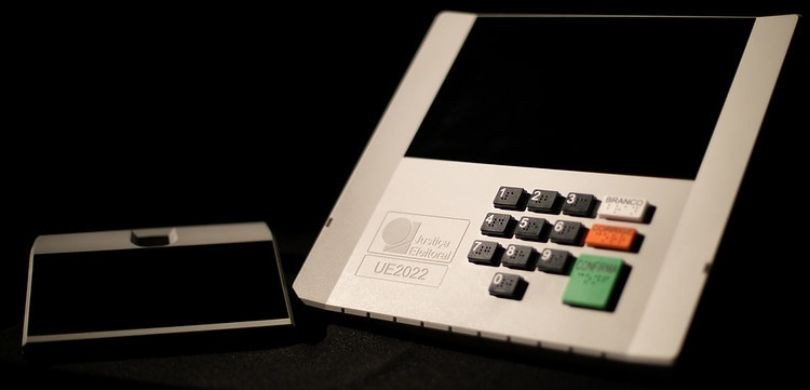 Fotografia na qual se vê um terminal de votação da urna eletrônica do modelo UE2022 e, ao lado e...