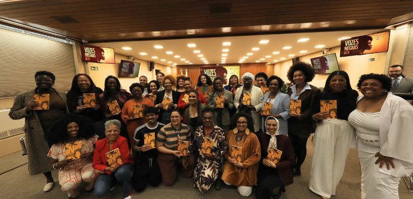 Fotografia de diversas pessoas, a maioria mulheres negras, posando sorrindo livros amarelos nas ...