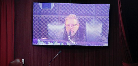 Fotografia de um homem falando em frente a um grupo de pessoas em um auditório. Ele usa uma blus...