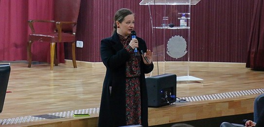 Fotografia de um homem falando em frente a um grupo de pessoas em um auditório. Ele usa uma blus...