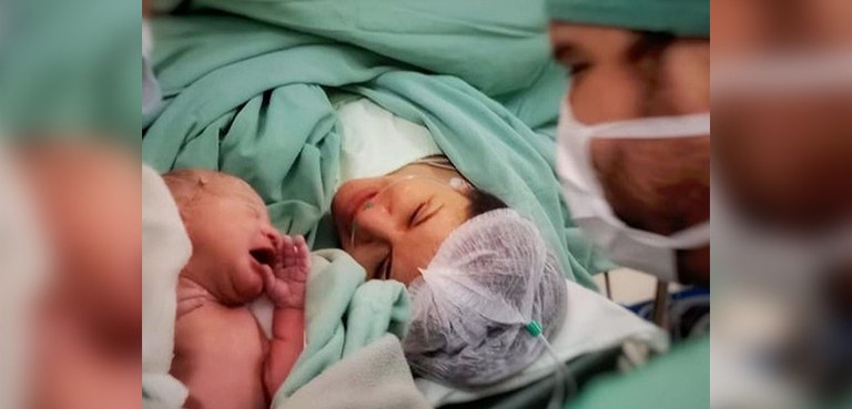 Servidoras da Justiça Eleitoral do Paraná falam da sua relação com a maternidade 3 Fotografia de uma mulher na maternidade, deitada em uma maca, olhando para sua filha recém-nasci...