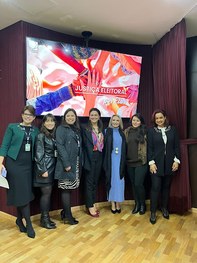 Fotografia de um grupo de pessoas posando para foto no palco de um auditório. Um homem e uma mul...